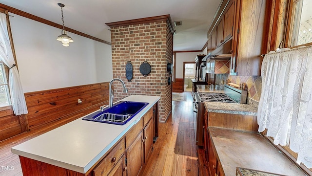 kitchen with a wainscoted wall, light countertops, hanging light fixtures, and a sink