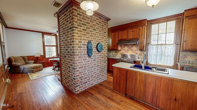 kitchen featuring light countertops, light wood-style flooring, stove, a sink, and under cabinet range hood