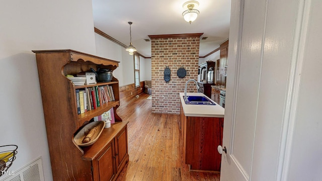 kitchen with visible vents, light countertops, light wood-style flooring, ornamental molding, and a sink