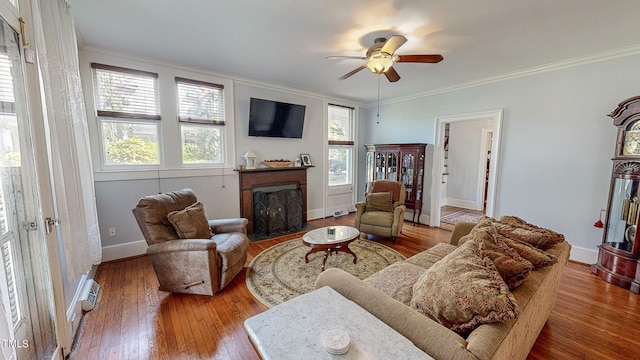 living room featuring baseboards, a ceiling fan, a fireplace with flush hearth, ornamental molding, and wood finished floors