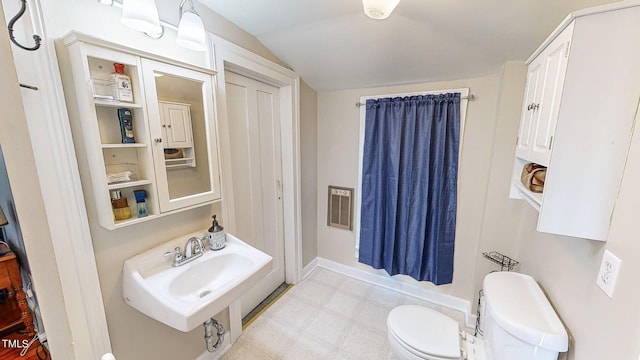 bathroom with heating unit, lofted ceiling, toilet, a sink, and tile patterned floors