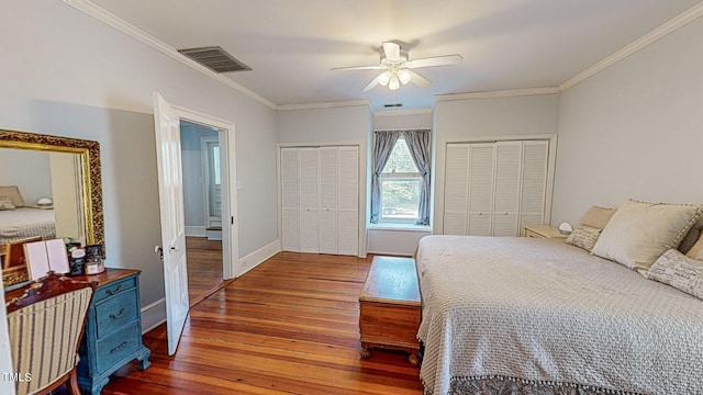 bedroom with two closets, baseboards, visible vents, and wood finished floors