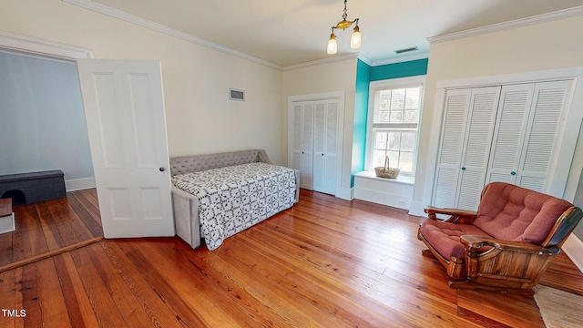 bedroom featuring wood finished floors, two closets, visible vents, and crown molding