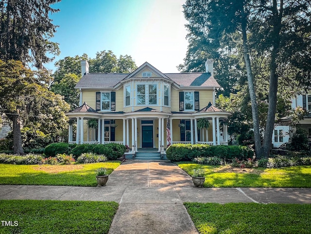 victorian-style house with covered porch, a front lawn, and a chimney