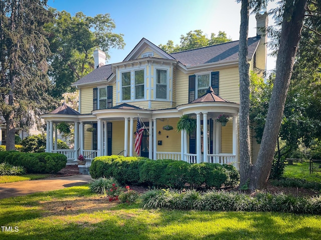 victorian-style house featuring covered porch, a chimney, and a front lawn