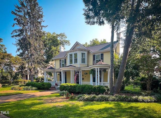 victorian-style house featuring a porch, a front yard, and a chimney