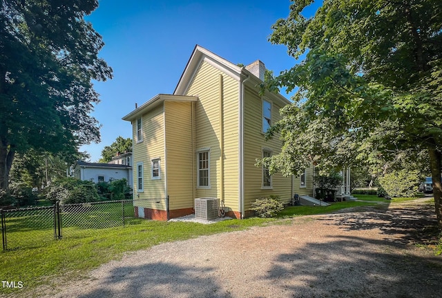 view of side of home featuring a yard, central AC, fence, and a chimney