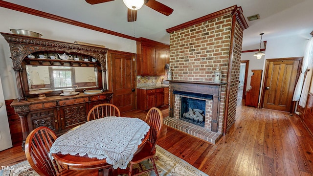 dining room featuring a brick fireplace, brick wall, ceiling fan, wood-type flooring, and ornamental molding