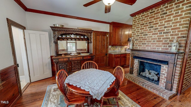 dining room featuring ornamental molding, a fireplace, light wood-style floors, and ceiling fan