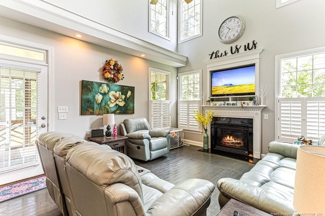 living room featuring dark hardwood / wood-style flooring, ceiling fan, a towering ceiling, and a healthy amount of sunlight