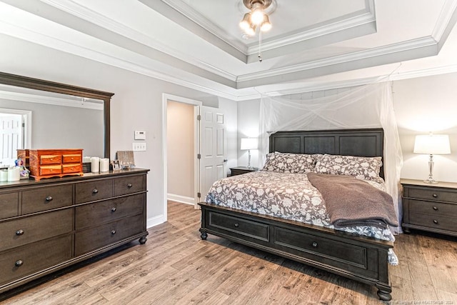 bedroom with crown molding, a tray ceiling, and light hardwood / wood-style flooring