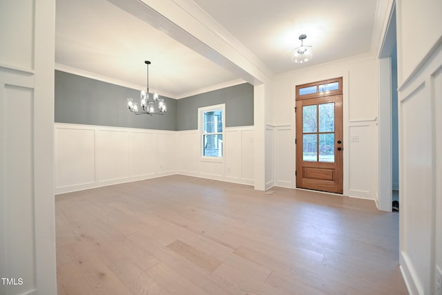 foyer with ornamental molding, light hardwood / wood-style floors, and an inviting chandelier