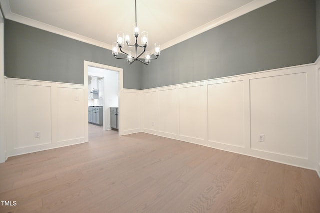 empty room with crown molding, light hardwood / wood-style flooring, and an inviting chandelier