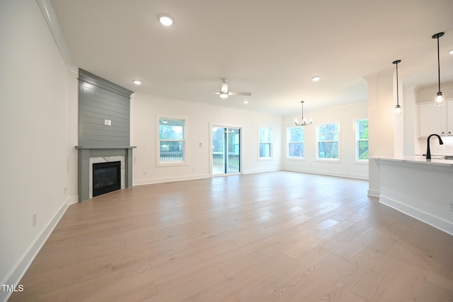 unfurnished living room featuring a high end fireplace, ceiling fan with notable chandelier, crown molding, sink, and light hardwood / wood-style flooring