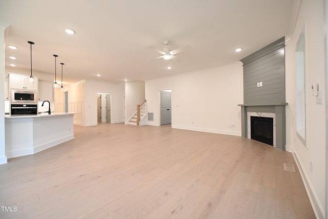 unfurnished living room featuring sink, light wood-type flooring, ceiling fan, and a premium fireplace