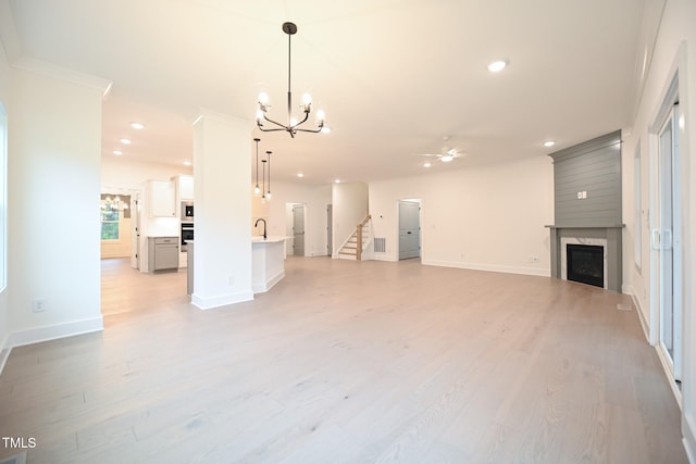 unfurnished living room with ceiling fan with notable chandelier, light hardwood / wood-style floors, sink, and crown molding