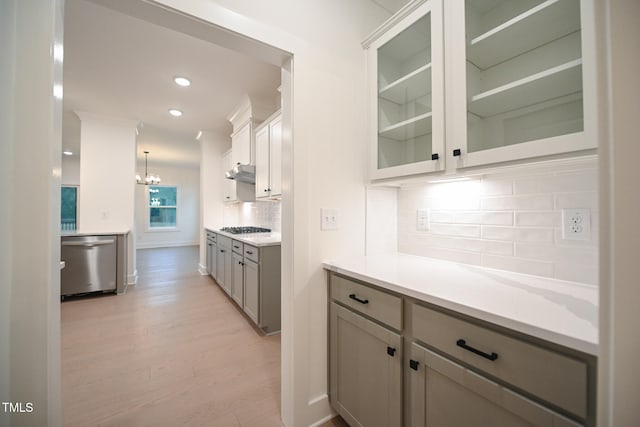 kitchen with stainless steel appliances, a notable chandelier, backsplash, pendant lighting, and light wood-type flooring