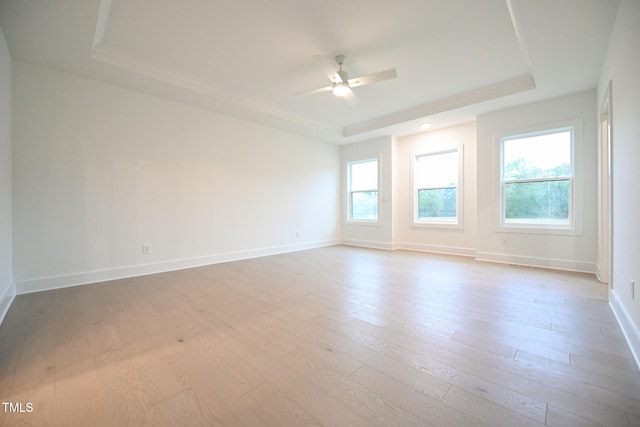 spare room with light wood-type flooring, a tray ceiling, and ceiling fan