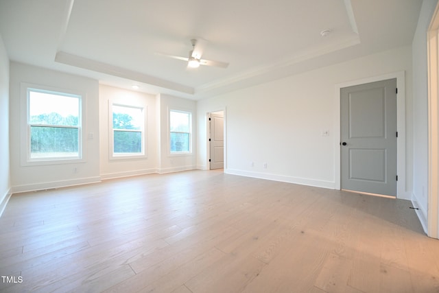 empty room featuring a raised ceiling, ceiling fan, and light hardwood / wood-style floors