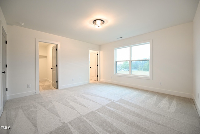 unfurnished bedroom featuring light colored carpet, a spacious closet, and a closet