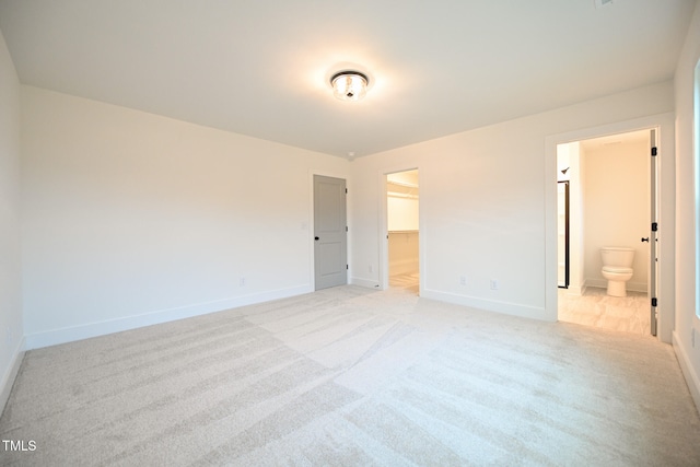 unfurnished bedroom featuring connected bathroom, a spacious closet, a closet, and light carpet