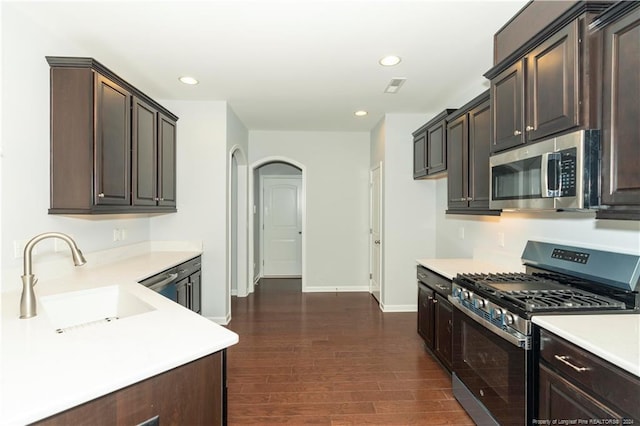 kitchen featuring appliances with stainless steel finishes, dark brown cabinetry, sink, and dark wood-type flooring