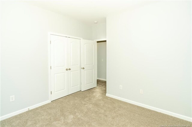 unfurnished bedroom with light colored carpet and a closet