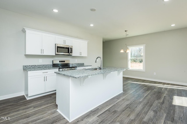 kitchen featuring stainless steel appliances, white cabinets, a sink, an island with sink, and light stone countertops