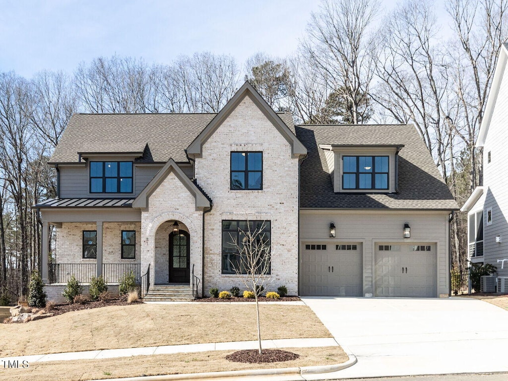 view of front of property featuring a garage, brick siding, driveway, roof with shingles, and a standing seam roof