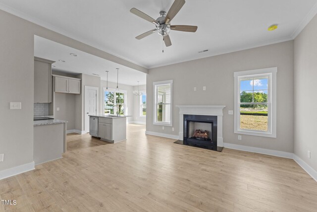 unfurnished living room featuring plenty of natural light, crown molding, ceiling fan with notable chandelier, and light hardwood / wood-style flooring