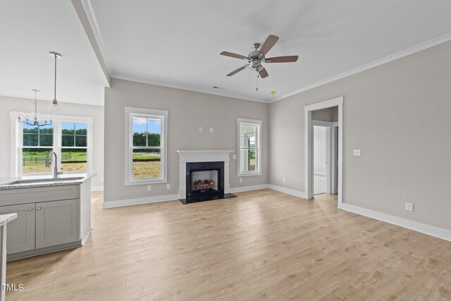 unfurnished living room with crown molding, sink, ceiling fan with notable chandelier, and light hardwood / wood-style flooring