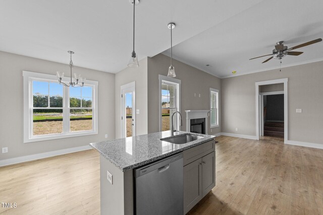 kitchen with an island with sink, dishwasher, pendant lighting, light stone counters, and sink