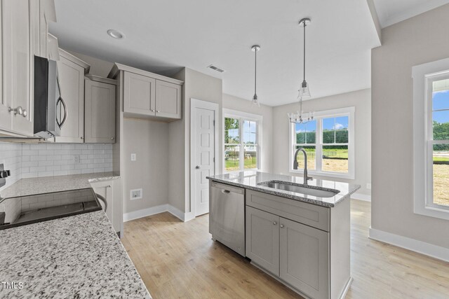 kitchen with light stone countertops, decorative light fixtures, stainless steel appliances, sink, and a center island with sink