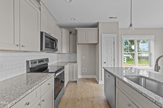 kitchen featuring backsplash, pendant lighting, sink, light stone countertops, and stainless steel appliances