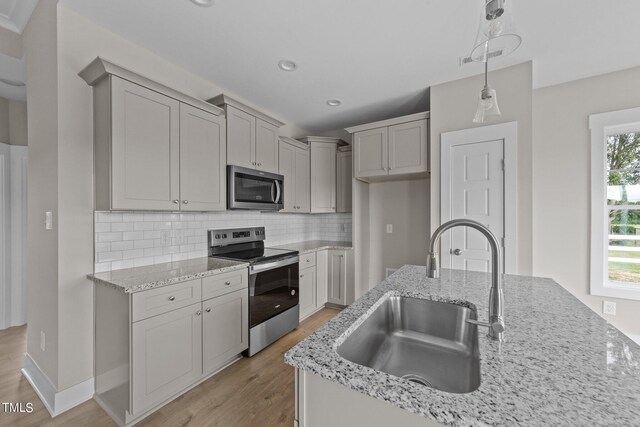 kitchen with appliances with stainless steel finishes, decorative light fixtures, tasteful backsplash, sink, and light hardwood / wood-style flooring