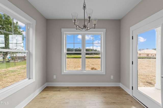 unfurnished dining area featuring light hardwood / wood-style floors, a wealth of natural light, and an inviting chandelier