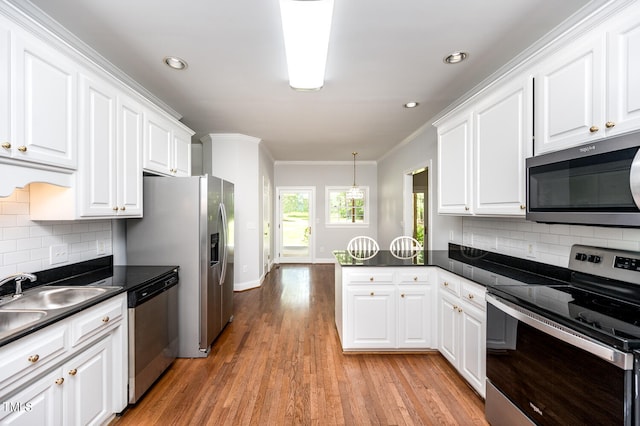 kitchen with light hardwood / wood-style flooring, kitchen peninsula, appliances with stainless steel finishes, decorative backsplash, and ornamental molding