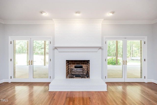 unfurnished living room featuring crown molding, french doors, light wood-type flooring, a brick fireplace, and brick wall