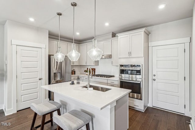 kitchen featuring stainless steel appliances, sink, an island with sink, dark hardwood / wood-style floors, and decorative light fixtures