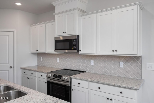 kitchen with white cabinets, stainless steel appliances, light stone counters, and backsplash