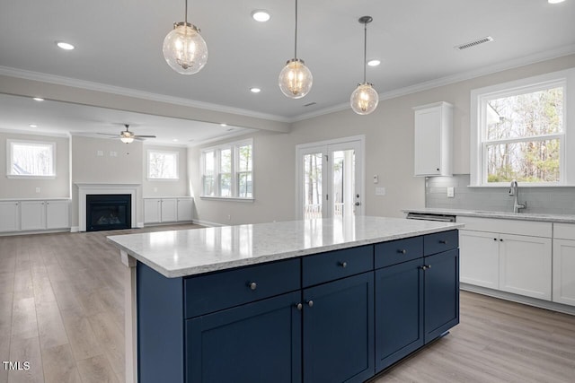 kitchen with visible vents, blue cabinetry, light wood-type flooring, and ornamental molding