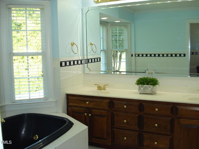 bathroom featuring plenty of natural light, tiled tub, and vanity