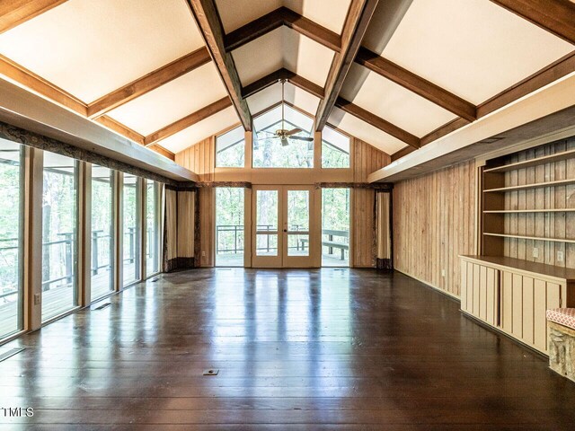 unfurnished room with wood walls, french doors, ceiling fan, dark hardwood / wood-style floors, and lofted ceiling with beams