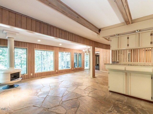 kitchen featuring a wood stove, beam ceiling, a notable chandelier, and wooden walls