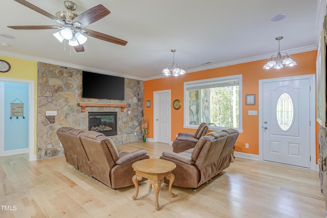 living area featuring ceiling fan with notable chandelier, light wood-style floors, a fireplace, crown molding, and baseboards