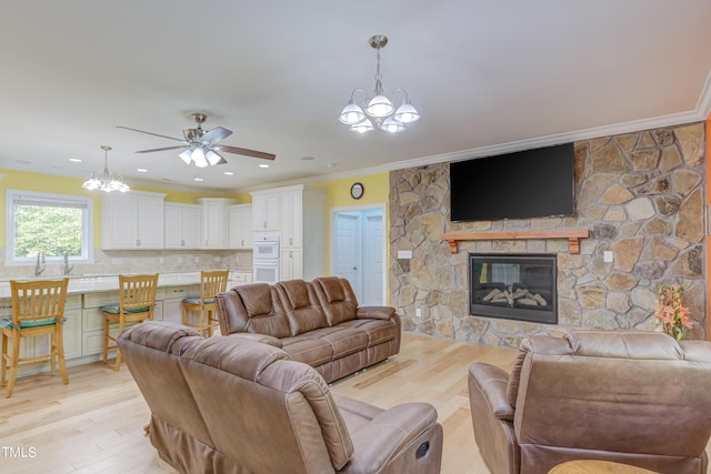 living area featuring light wood-type flooring, ornamental molding, a stone fireplace, recessed lighting, and ceiling fan with notable chandelier