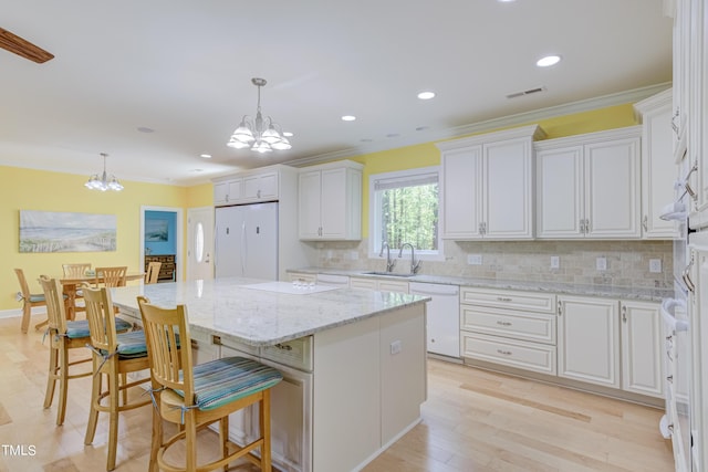 kitchen with white appliances, visible vents, a kitchen island, an inviting chandelier, and white cabinets