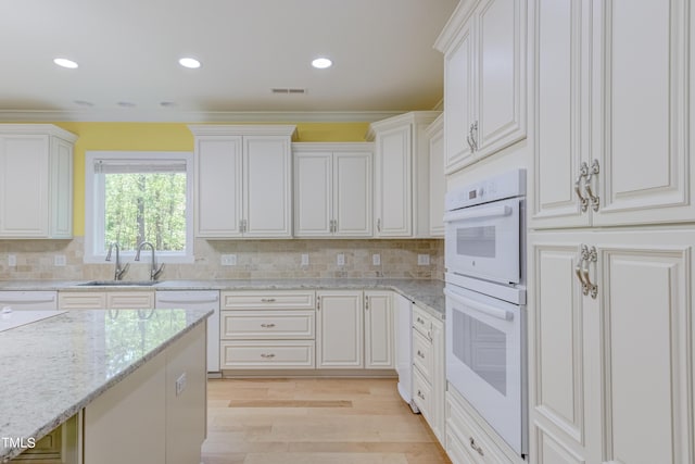 kitchen featuring white appliances, visible vents, light wood finished floors, a sink, and decorative backsplash