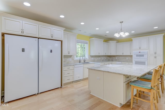 kitchen with pendant lighting, a sink, backsplash, white cabinetry, and white appliances