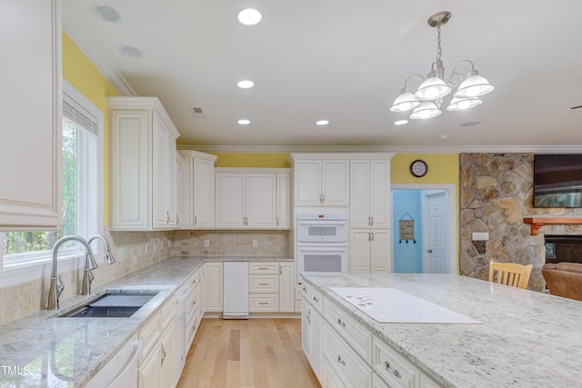 kitchen with crown molding, light stone counters, white appliances, white cabinetry, and a sink